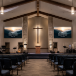 Modern church interior with a stage, illuminated cross and small LED screens on either side