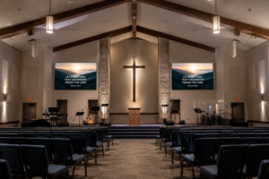 Modern church interior with a stage, illuminated cross and small LED screens on either side