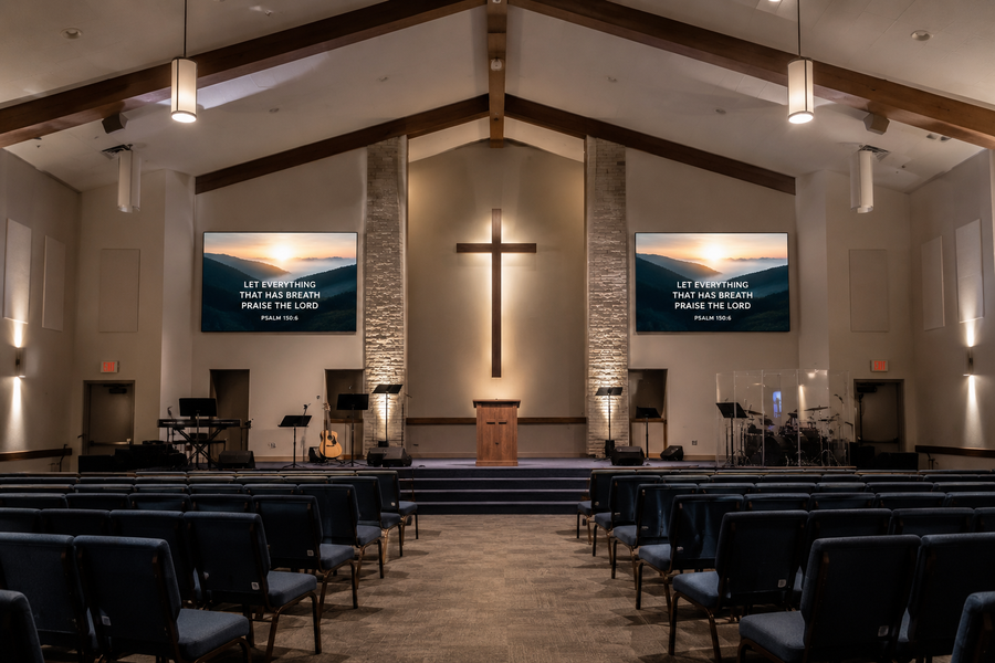 Modern church interior with a stage, illuminated cross and small LED screens on either side